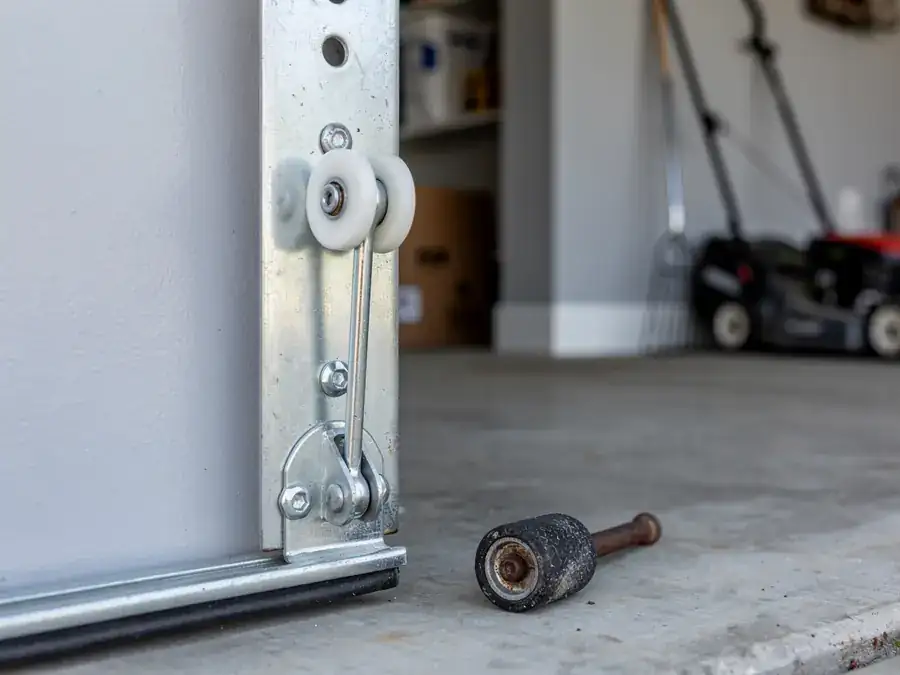 A garage door roller is attached to the door, and a broken roller lies on the floor.