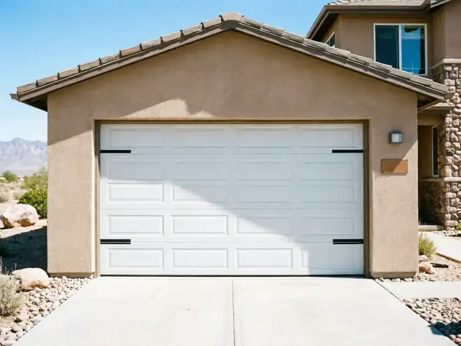 A white garage door with decorative black hardware on a stucco house.